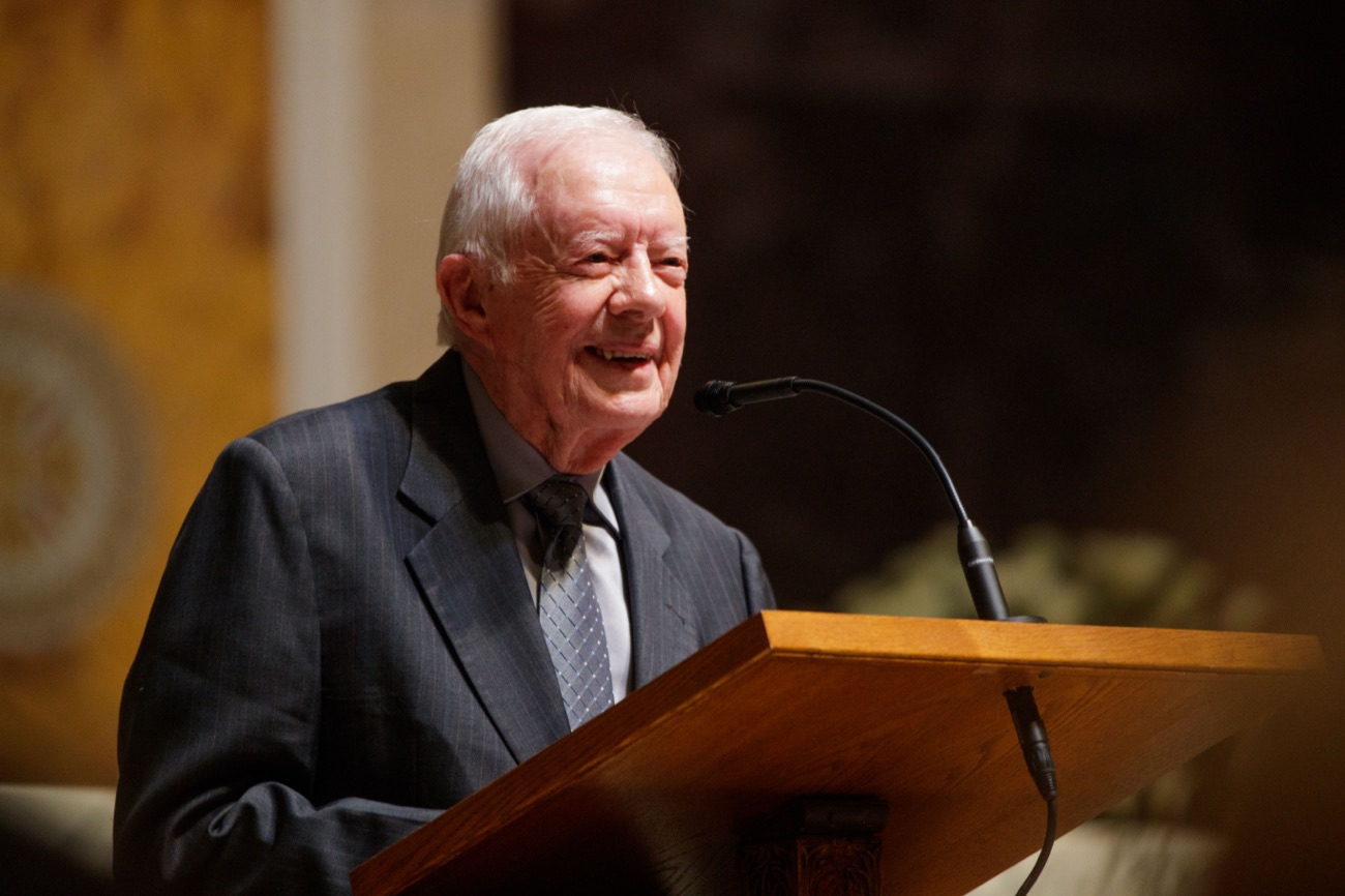 Former President Jimmy Carter smiles at a wooden podium.