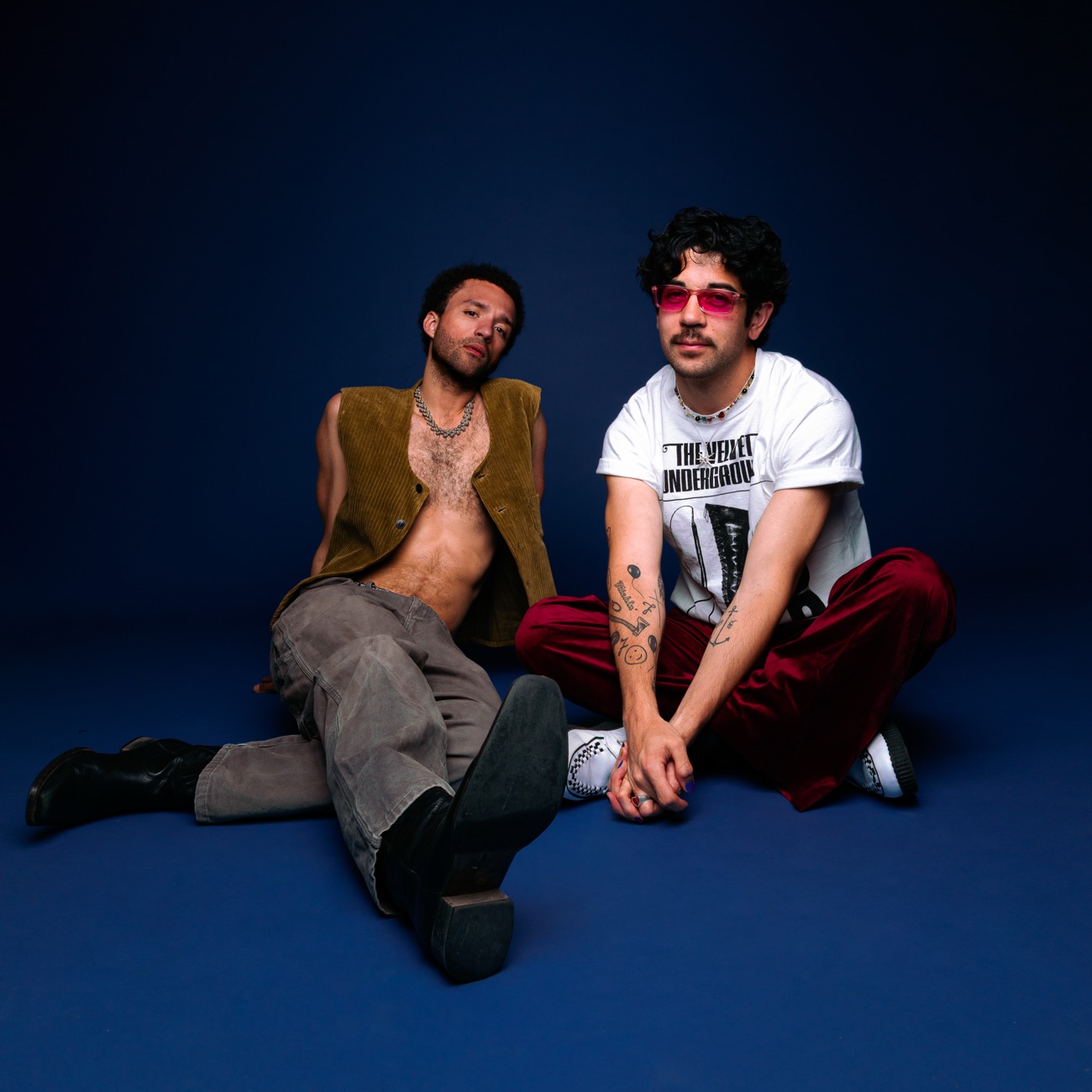 The two members of Firemill sit on the floor of a deep-blue studio set.