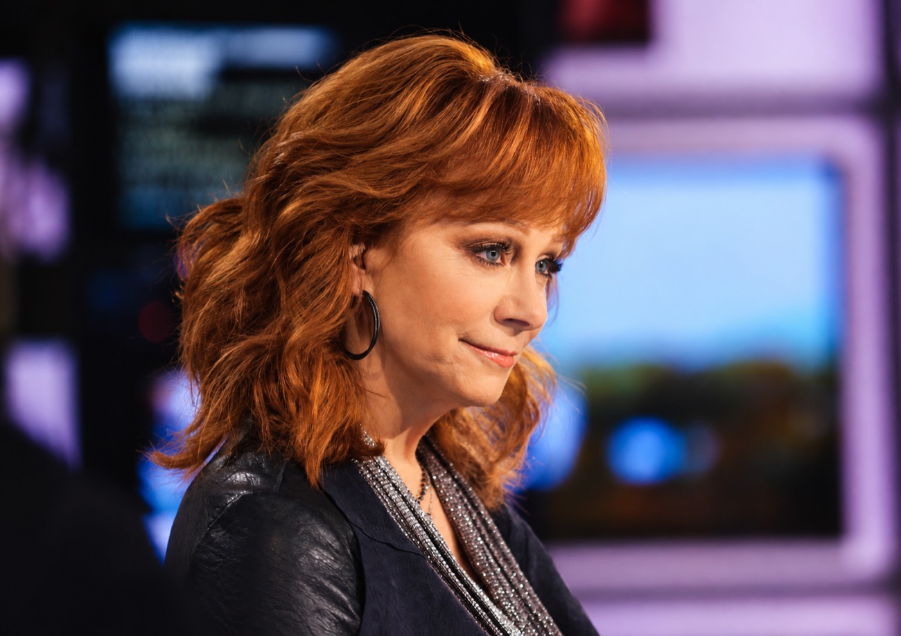 Reba McEntire looks down with a half smile on a television set.