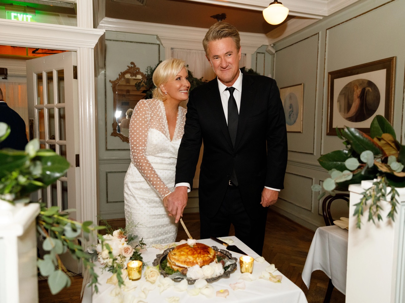 A bride in white lace and her groom cut the cake at a candlelit reception.